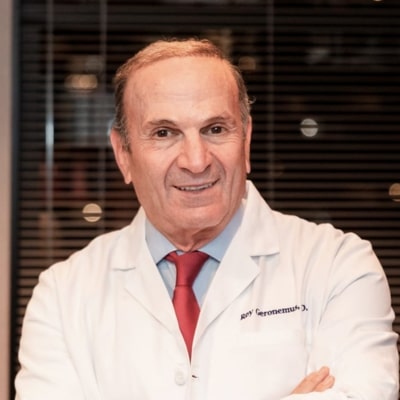 Experienced male dermatologist in white lab coat and red tie, expert in skincare and anti-aging treatments, professional medical office background.